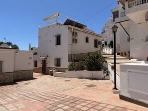 A narrow street with white buildings, a tiled pavement, and a staircase leading to a higher level.
