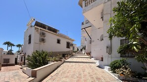Una calle estrecha con baldosas de terracota, edificios blancos con balcones y macetas con plantas.