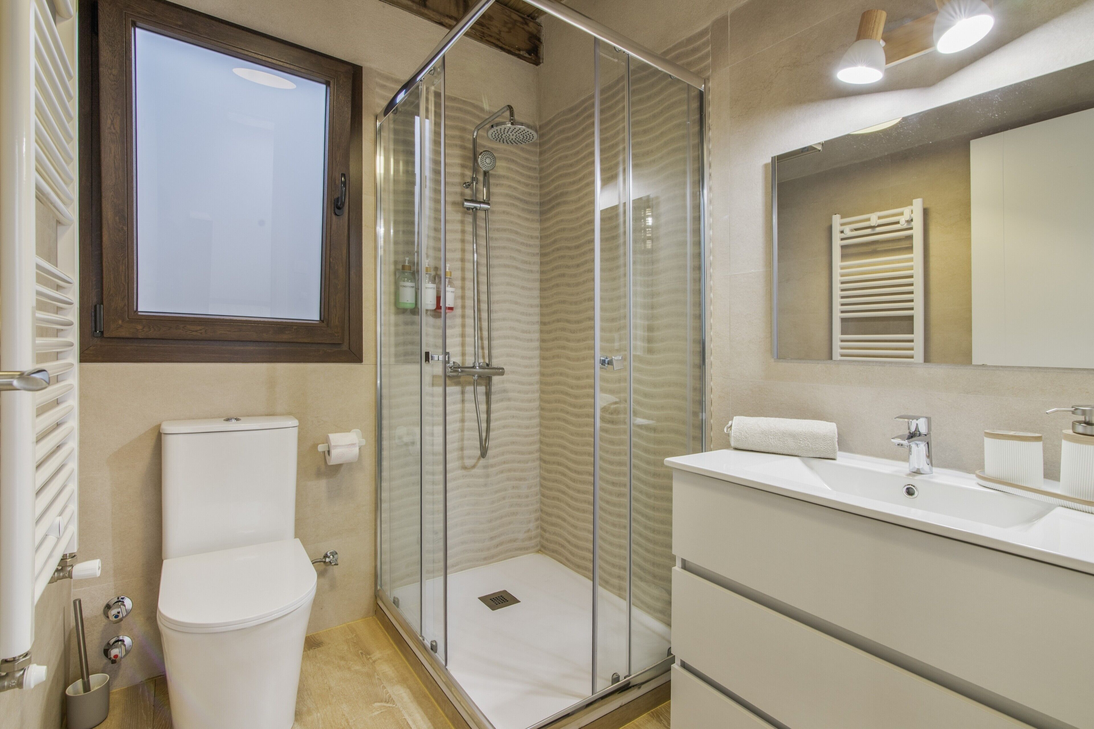 A bathroom with a glass-enclosed shower, a toilet, a sink, and a mirror.