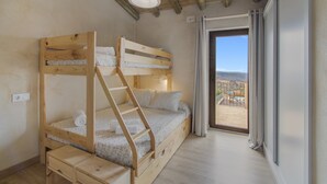 A bunk bed room with a wooden ladder, a small wooden desk, and a view of the outdoors through a sliding door.