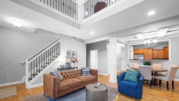 A spacious living room with a brown sofa, blue armchairs, and a round coffee table. A staircase with a railing leads to an upper level. - Hilltop 3BR for 10, Private Garage, Skyline Views (Covington)