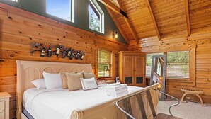 Une chambre à coucher de style cabane en bois, avec un grand lit, une tête de lit en bois, un porte-bouteilles fixé au mur et un banc en bois.