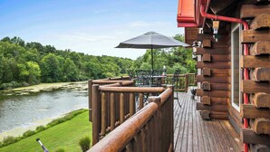 Une terrasse en bois avec vue sur la rivière, des meubles d’extérieur et un grand parasol.