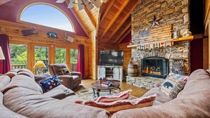 Un intérieur chaleureux de chalet en bois avec une cheminée en pierre, des sièges confortables et un grand téléviseur.