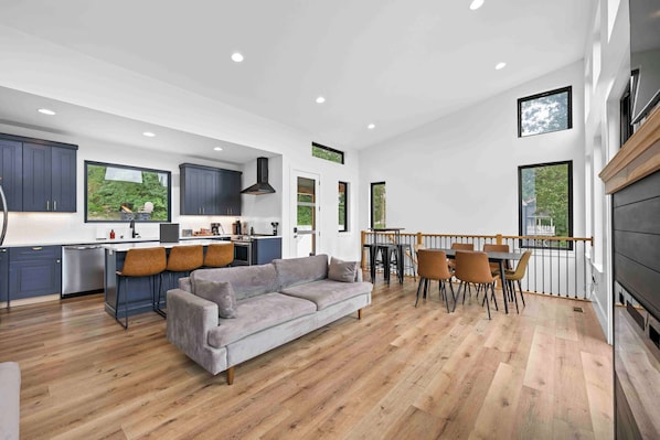A spacious kitchen with dark cabinets, a gray sofa, and a dining area with wooden flooring and chairs. - Lakefront Home with Dock - Hot tub - 7 miles to Ark (Williamstown)