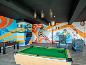 A billiards table, a foosball table, and a mural with sports themes.