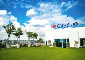 A rooftop terrace with outdoor seating, a view of the city, and a building with 'I ♥ CityBlue' signage.