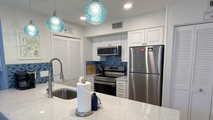 Una cocina moderna con armarios blancos, electrodomésticos de acero inoxidable, una cafetera y elegantes lámparas colgantes de vidrio azul.