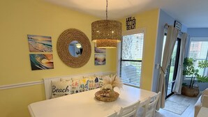 Un comedor con una mesa blanca, sillas, un espejo tejido y decoración en la pared.