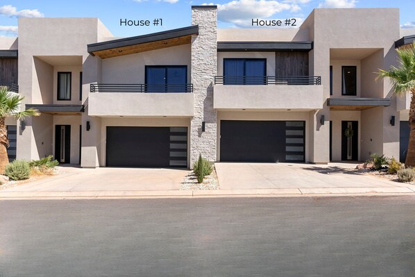 Un immeuble résidentiel moderne à deux étages, doté d’une façade en pierre, de deux garages et d’un balcon situé à l’étage supérieur.