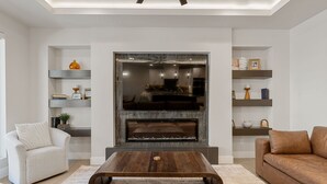 A modern living room with a fireplace, a sofa, a coffee table, and shelves with decorative items.