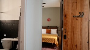 Habitación de hotel con cama, puerta de madera y baño visible a través de una puerta abierta.