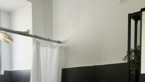 Un baño con inodoro blanco, zona de ducha con azulejos negros y lavamanos con espejo.
