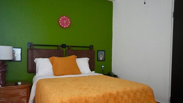 Ein Hotelzimmer mit einem Bett, einem Nachttisch, einer Lampe, einer Uhr und einem gerahmten Bild an der Wand.