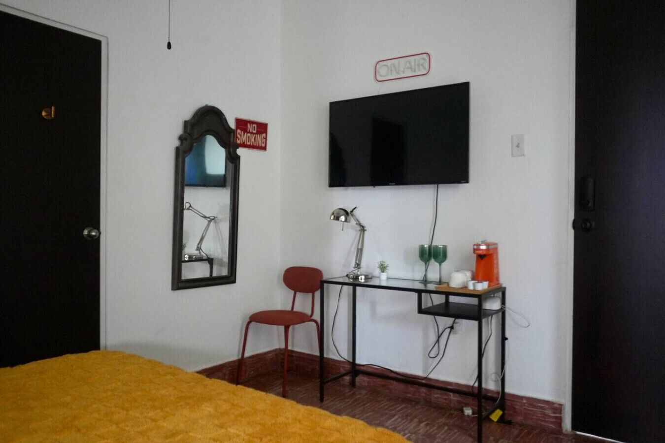 Una habitación con cama, escritorio con computadora, silla, televisor y un cartel que dice “NO FUMAR”.