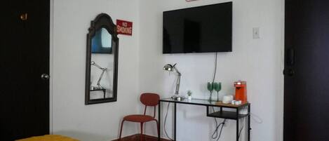 Una habitación con cama, escritorio con computadora, silla, televisor y un cartel que dice “NO FUMAR”.