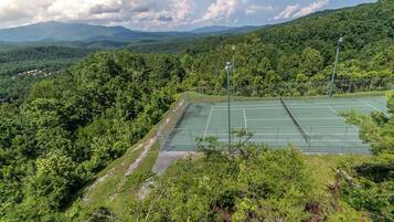 A tennis court surrounded by lush greenery and mountains in the background.