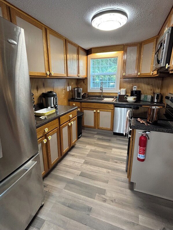 Cocina compacta con armarios de madera, electrodomésticos de acero inoxidable, una ventana con persianas y un extintor.