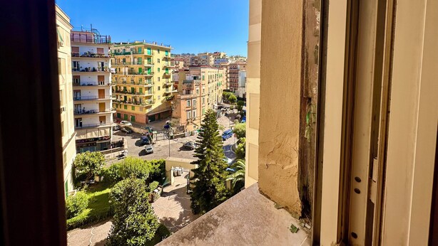 A view from a balcony overlooking a residential area with multi-story buildings, a parking lot, and greenery. - Giano's Room Napoli (Naples)