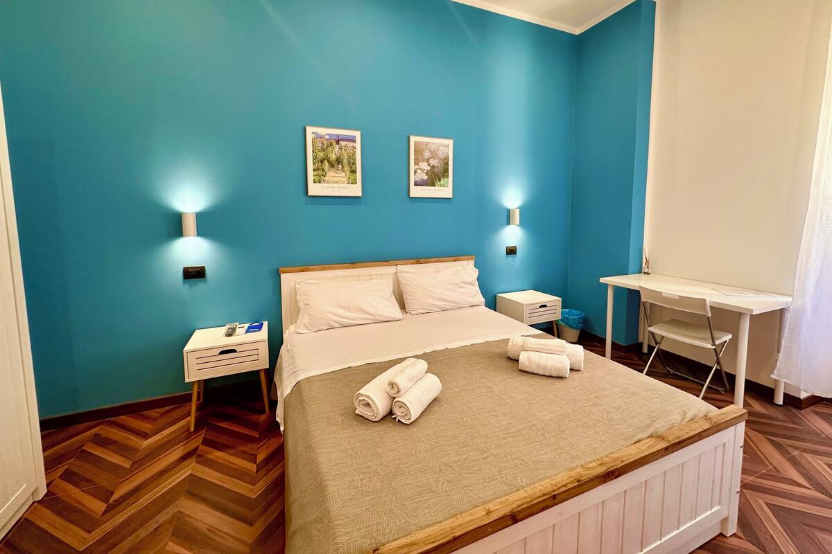 A bedroom with a bed, two wall-mounted lights, a desk, and a chair.