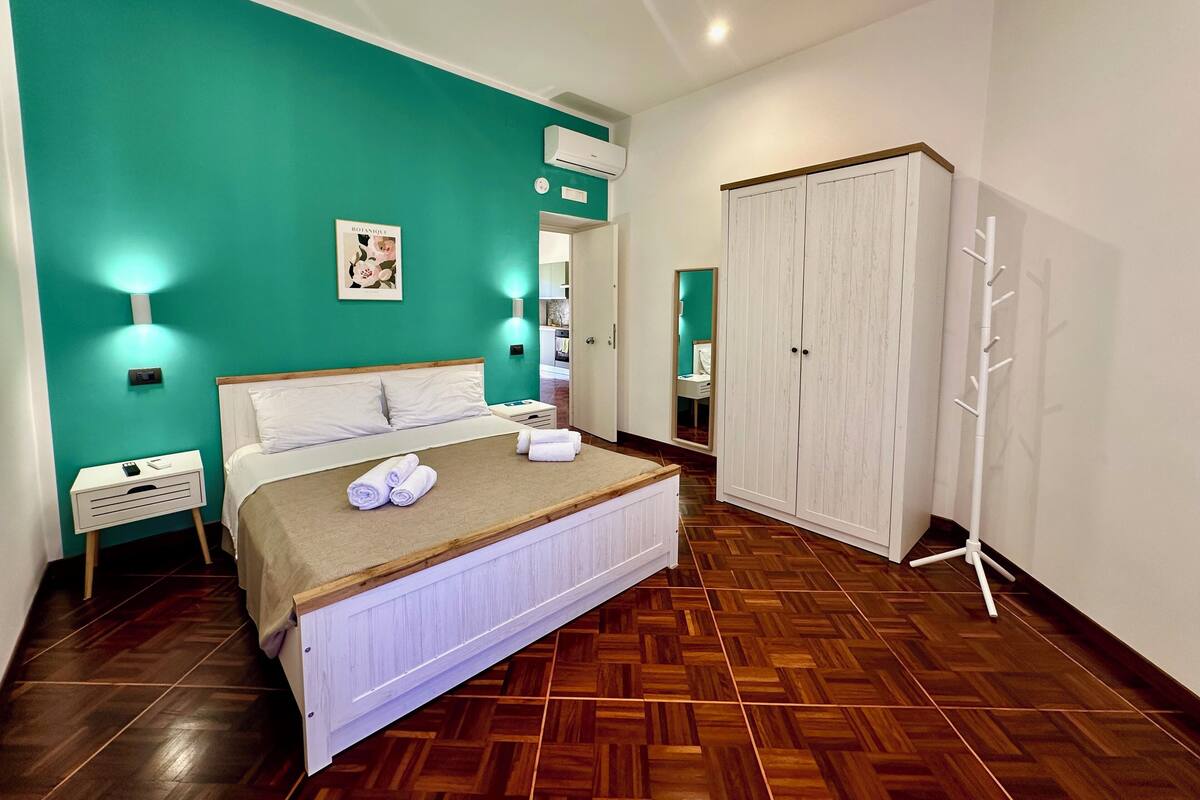 A bedroom with a bed, a nightstand, a wardrobe, and a bathroom visible through an open door.