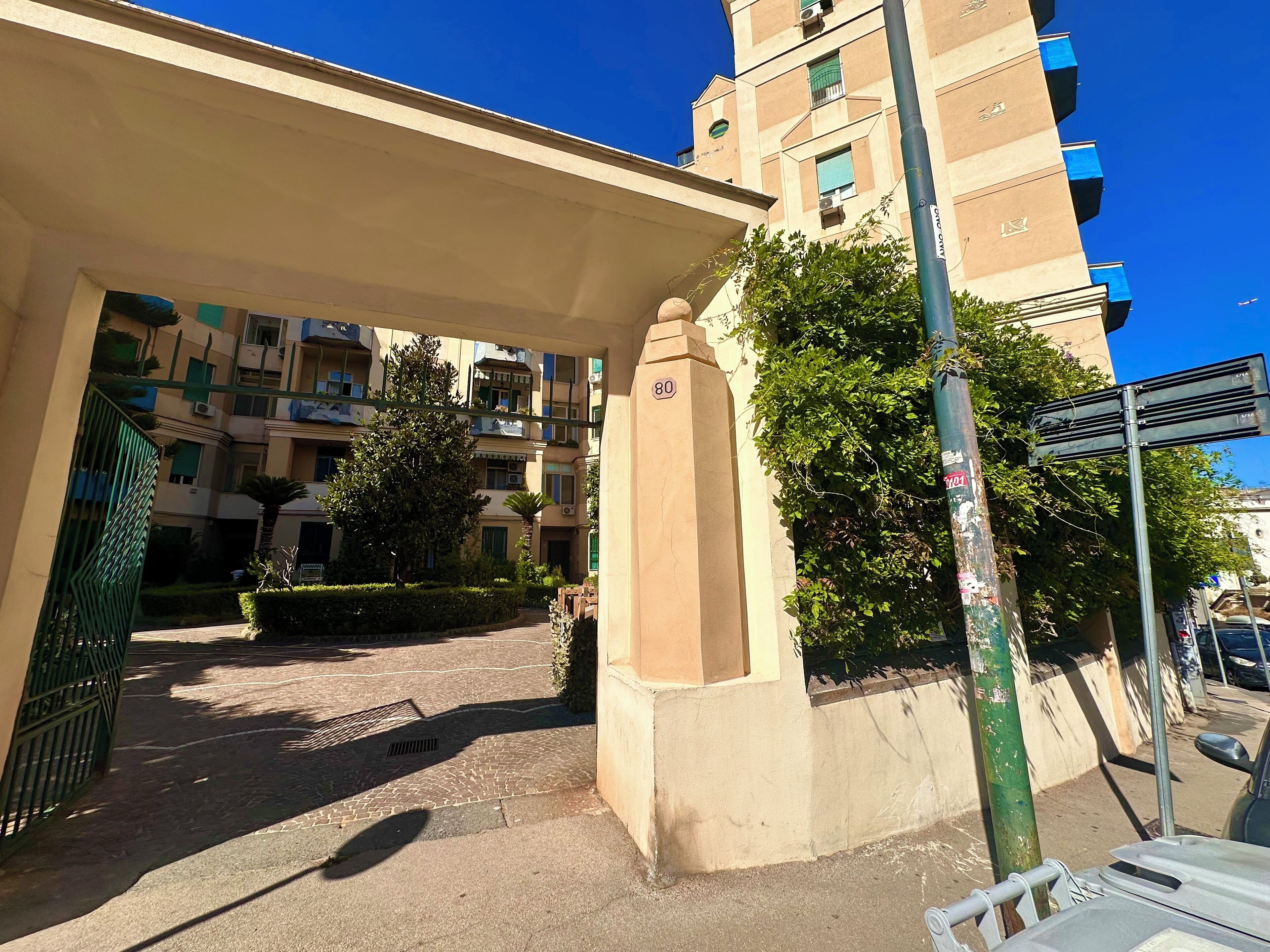 A multi-story residential building with balconies, a gated entrance, and a clear blue sky.