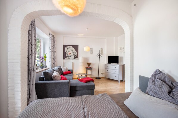 Une chambre à coucher moderne avec un lit, un canapé gris, une télévision et un bureau.