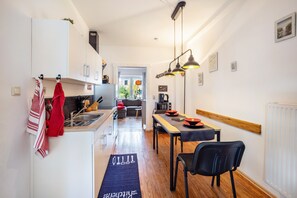 Une cuisine moderne avec un coin repas, donnant sur le salon, et un couloir menant à l’entrée.