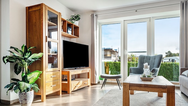 A modern living room with a television, wooden cabinet, and a large window with a view of the outside. - Apartment 'Kleine Auszeit - Hohe Lith' with Private Terrace, Balcony and Wi-Fi (Cuxhaven)