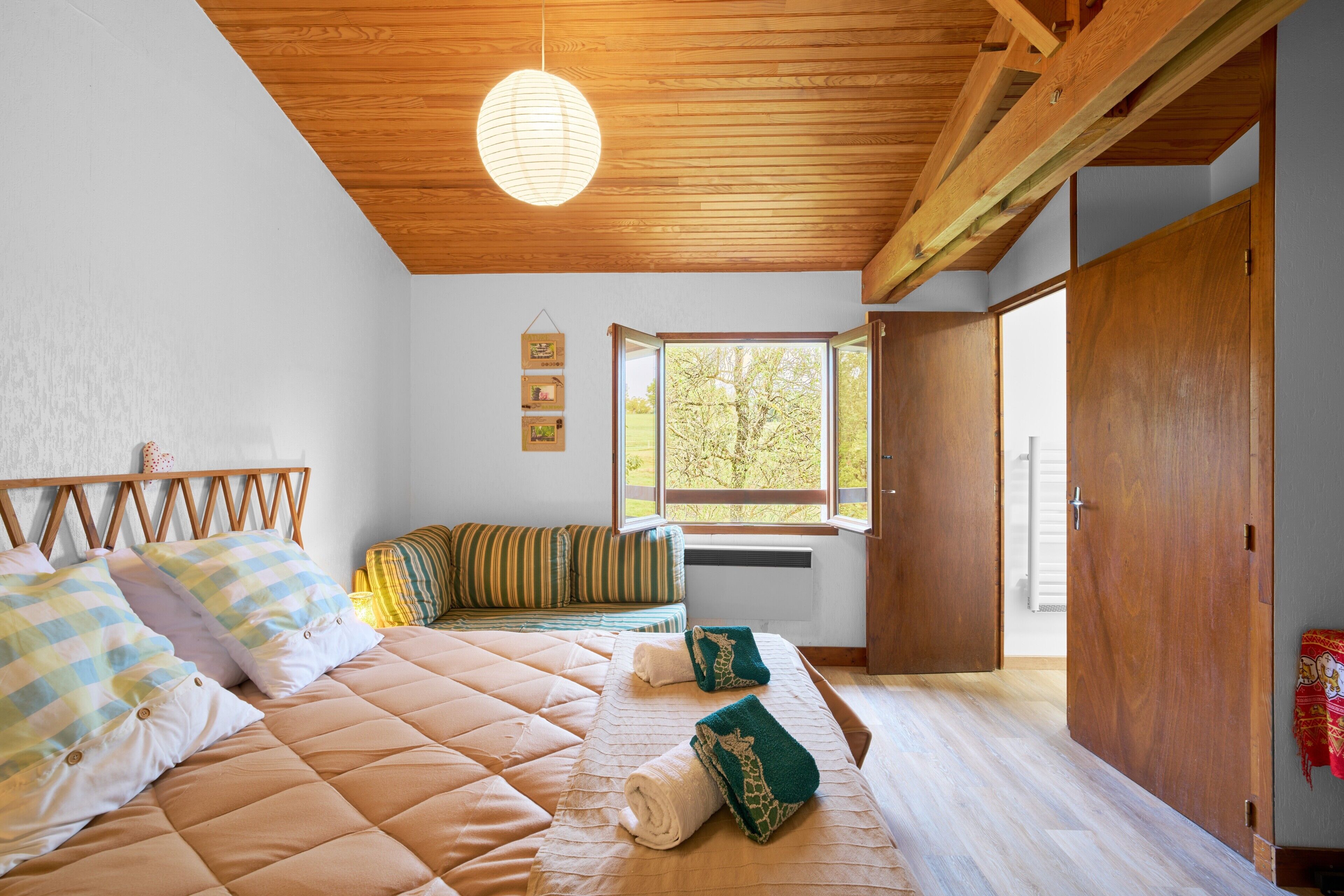 A bedroom with a bed, a window, a wooden ceiling, and a wardrobe.