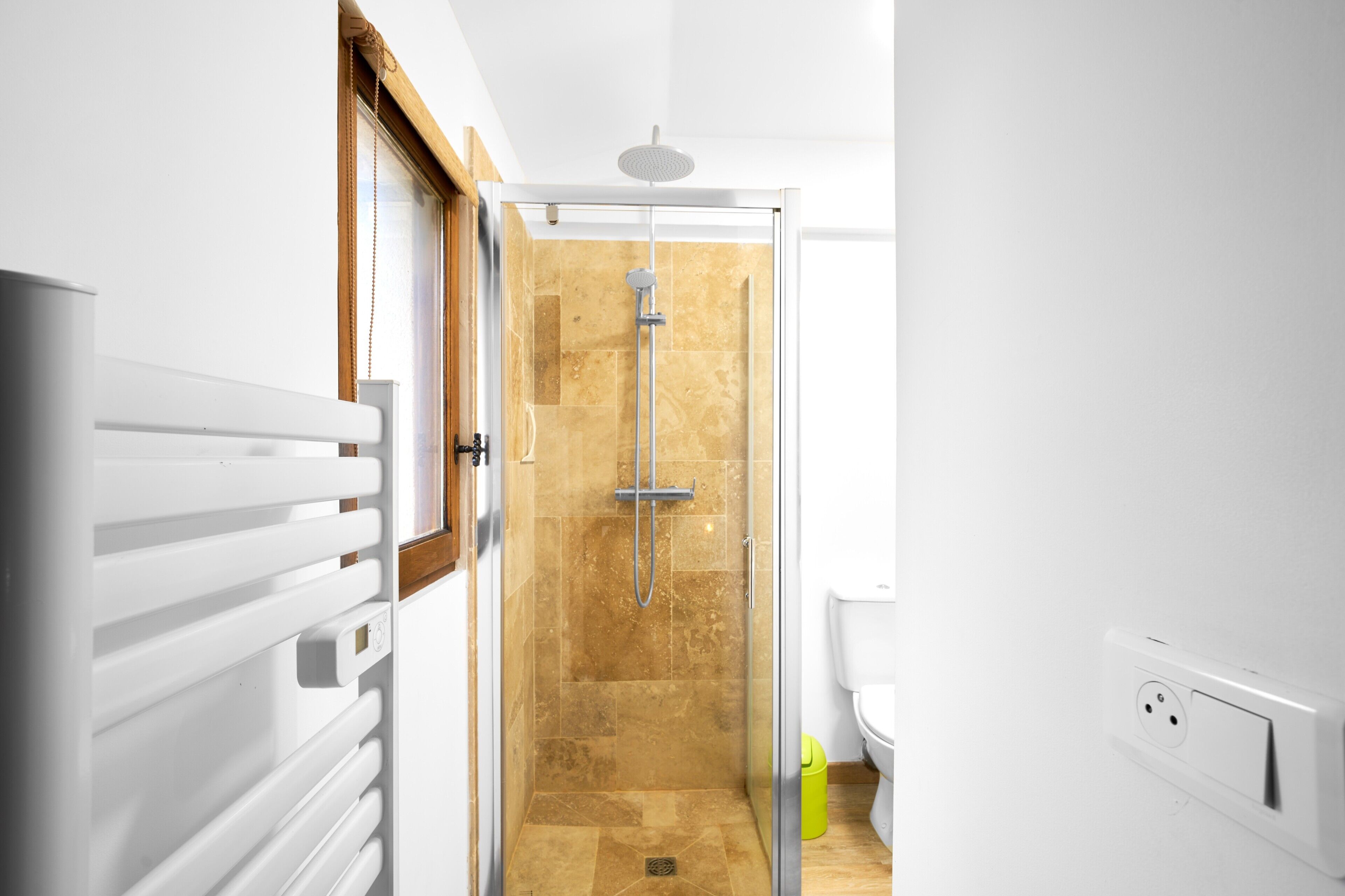 A modern bathroom with a glass shower enclosure, a white radiator, and a visible electrical outlet.