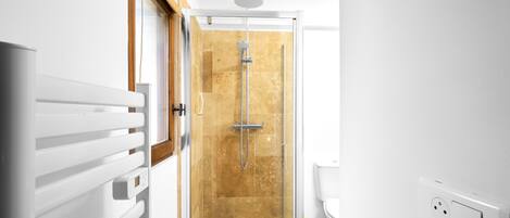 A modern bathroom with a glass shower enclosure, a white radiator, and a visible electrical outlet.
