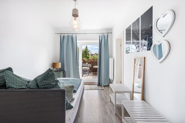 A bedroom with a bed, a bedside table, a lamp, a window with curtains, and a view of the outdoors. - Apartment 'Bella Verde' with Balcony and Wi-Fi (Lübeck)