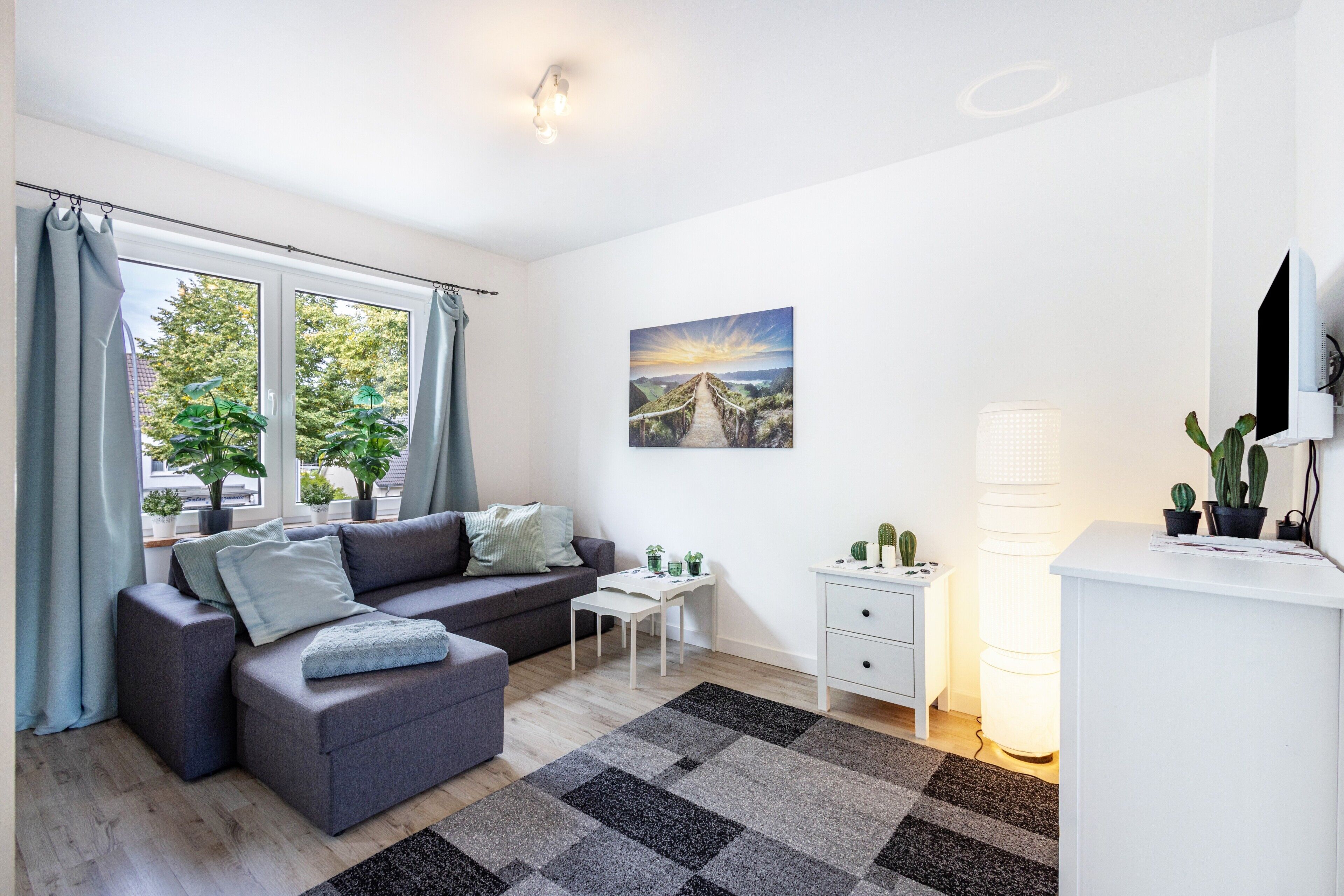 A modern living room with a sofa, a small table, a lamp, and a painting on the wall.