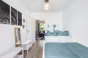 A bedroom with a bed, a bench, a mirror, and a door leading to another room. - Apartment 'Bella Verde' with Balcony and Wi-Fi (Lübeck)
