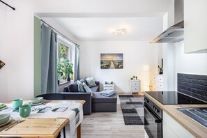 A modern kitchen with a stove, oven, and a dining area with a table set for two. - Apartment 'Bella Verde' with Balcony and Wi-Fi (Lübeck)