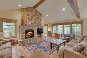 Un salón amplio con chimenea de piedra, ventanas grandes y asientos cómodos.
