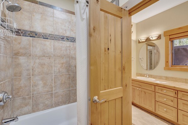 Un baño con bañera, ducha, tocador de madera y un espejo.