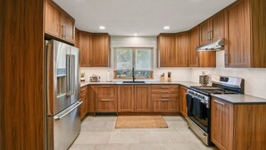 A modern kitchen with wooden cabinets, stainless steel appliances, and a window with blinds. - Iowa City 4br Backyard Walk To Stadium 4 Bedroom Home (Iowa City)