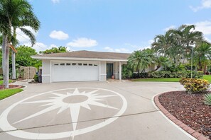 A residential house with a garage, palm trees, and a driveway with a compass design. - Gulf Tide Getaway 2 Bedroom Home (Bradenton)
