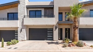 Una casa moderna de dos pisos con fachada de piedra, un garaje amplio y un jardín bien cuidado con una palmera.