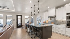 Cocina moderna con gabinetes blancos, una isla grande con taburetes, iluminación colgante y un salpicadero de baldosas en espiga.