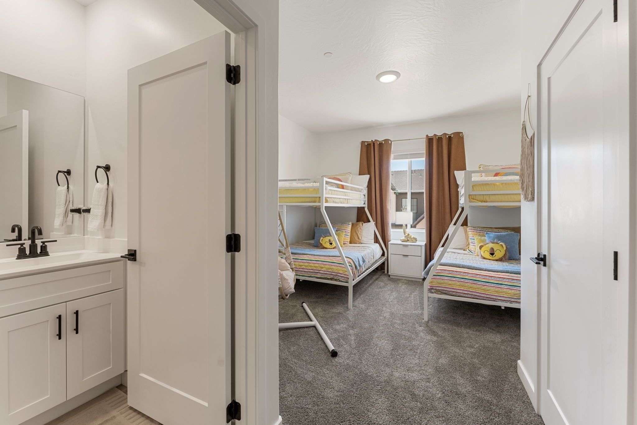 A bedroom with bunk beds, a white wardrobe, and a bathroom with a mirror and sink.