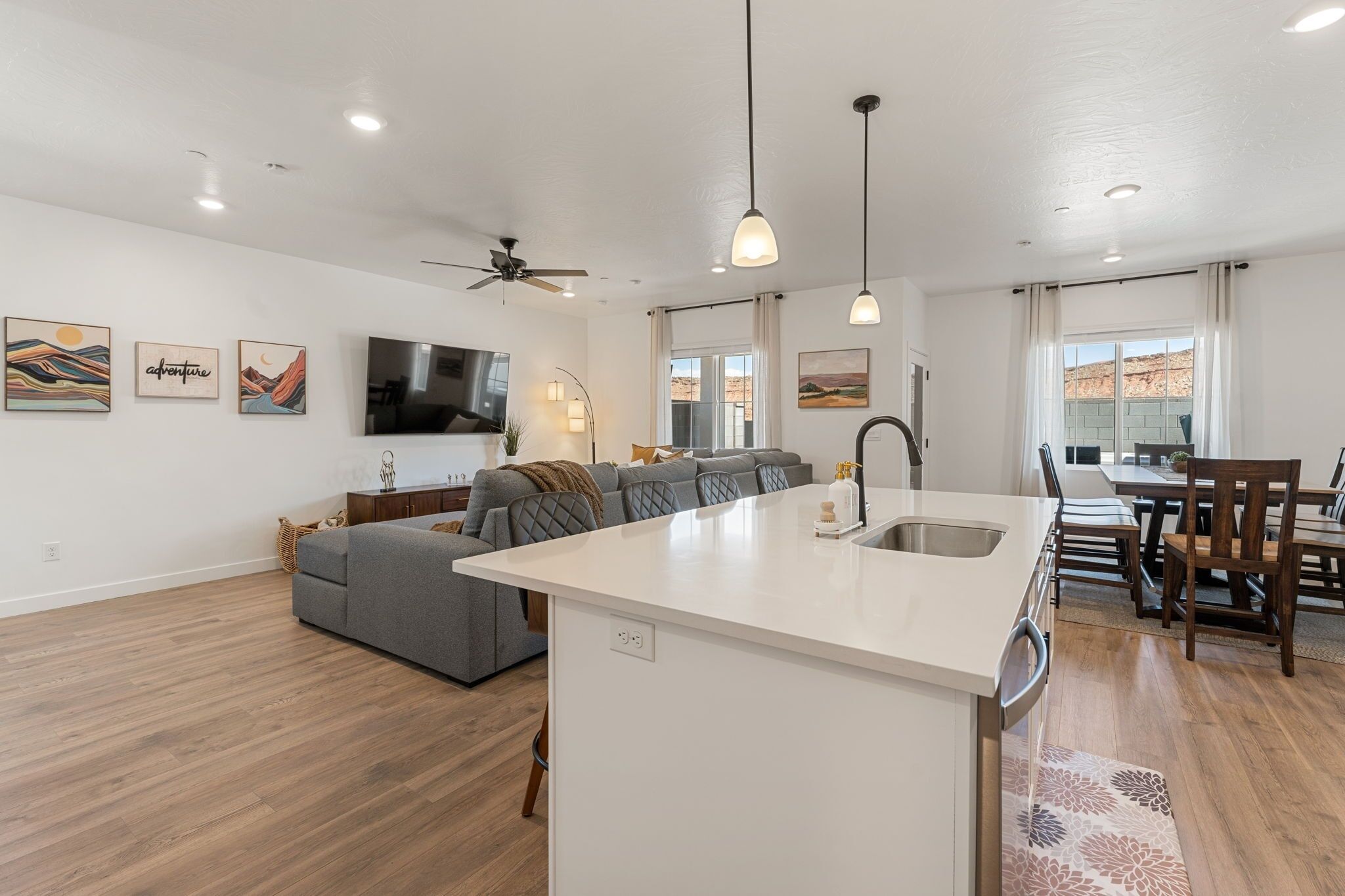 A modern kitchen with a central island, a dining area with wooden chairs, and a living room with a sofa and artwork.