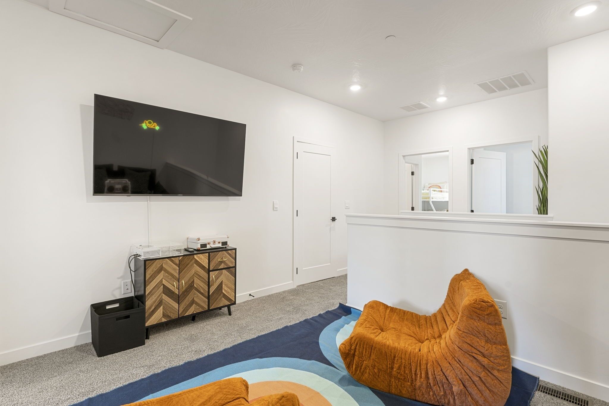 Una habitación moderna con un televisor de pantalla plana montado en la pared, un mueble de madera con diseño de espiga, un bote de basura negro y una alfombra colorida.