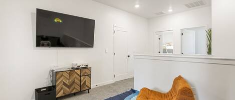 Una habitación moderna con un televisor de pantalla plana montado en la pared, un mueble de madera con diseño de espiga, un bote de basura negro y una alfombra colorida.