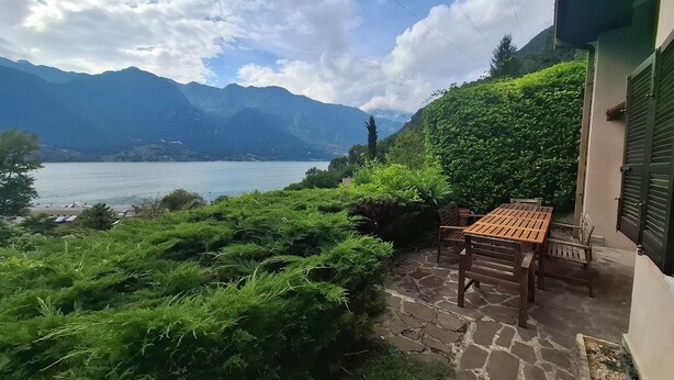 A patio with a table and chairs, overlooking a lake and mountains.
