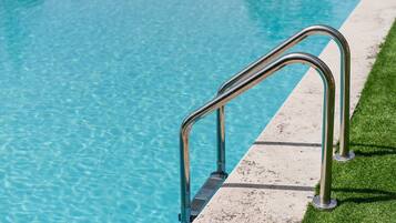A swimming pool with clear blue water and a metal handrail on the edge.