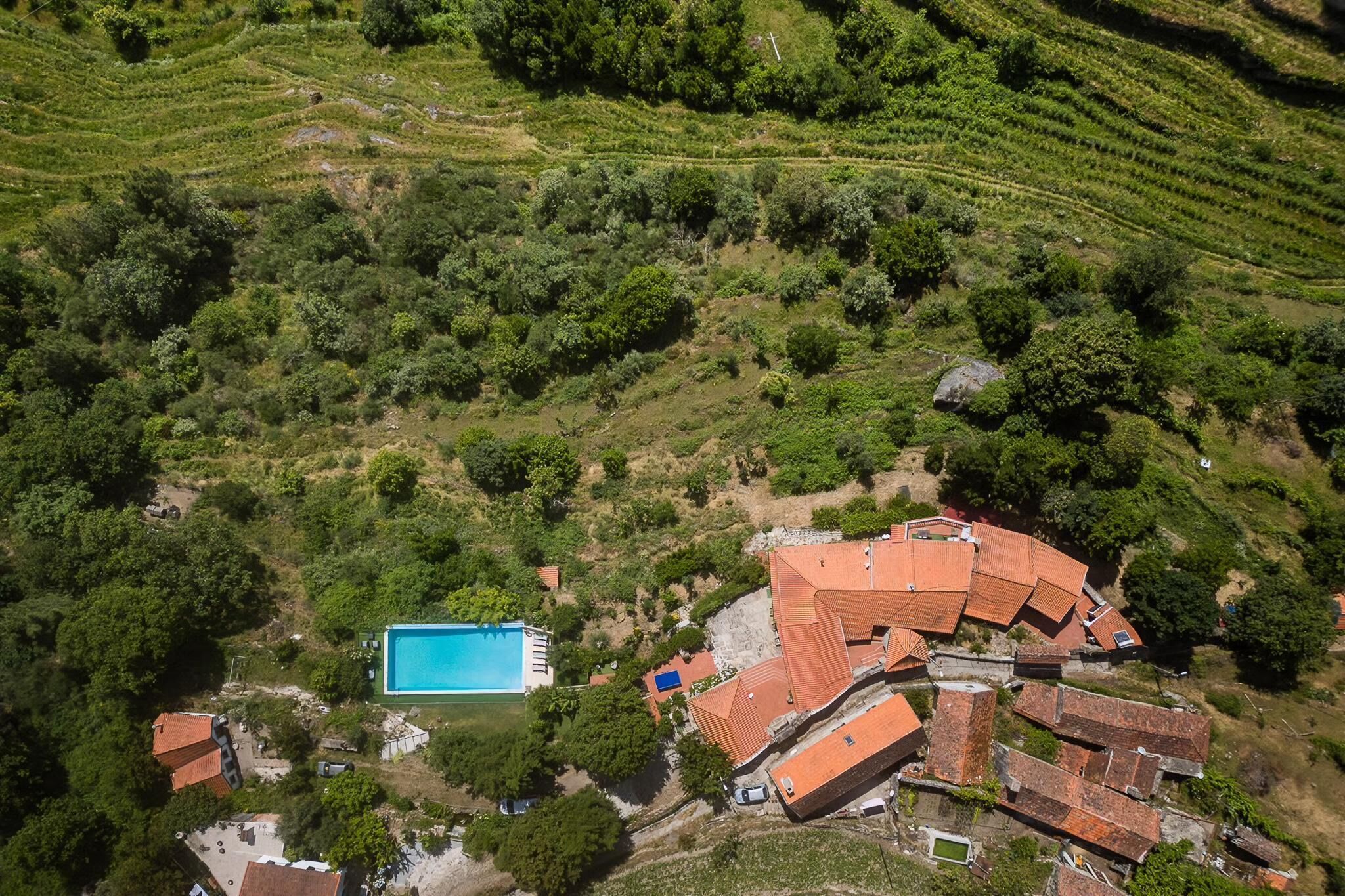 Vue aérienne d’une propriété située sur une colline, avec des jardins en terrasses, une piscine et des bâtiments traditionnels aux toits rouges.