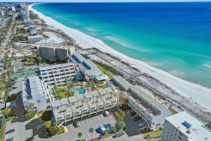 An aerial view of a coastal hotel with a beachside location, parking facilities, and a swimming pool.